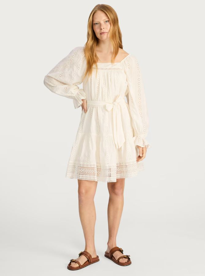 Model wearing an ivory eyelet mini dress with puff sleeves and a tie belt.
