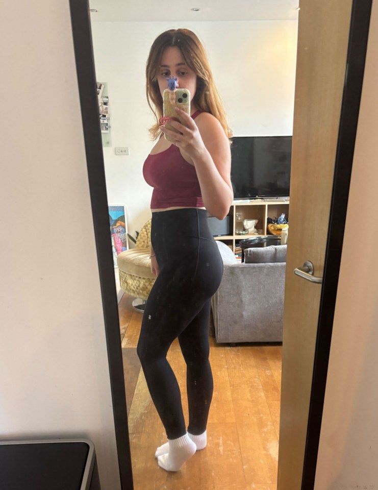 Woman in maroon top and black leggings reflected in a mirror.