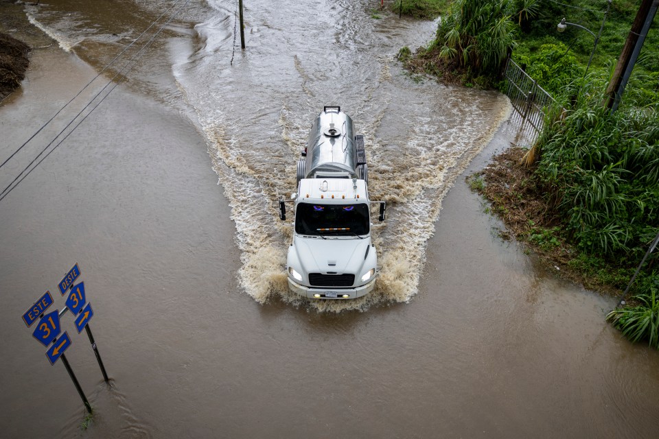 Truck driving through floodwaters on a road.