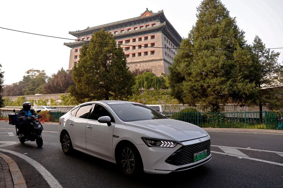 BYD electric vehicle driving on a Beijing street with a traditional Chinese building in the background.