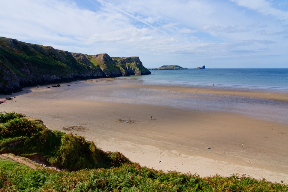 Virtually deserted beach at low tide with steep cliffs.