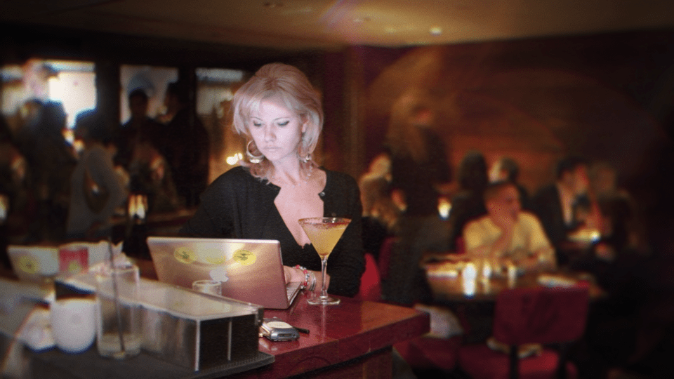 Woman using laptop at bar with cocktail.