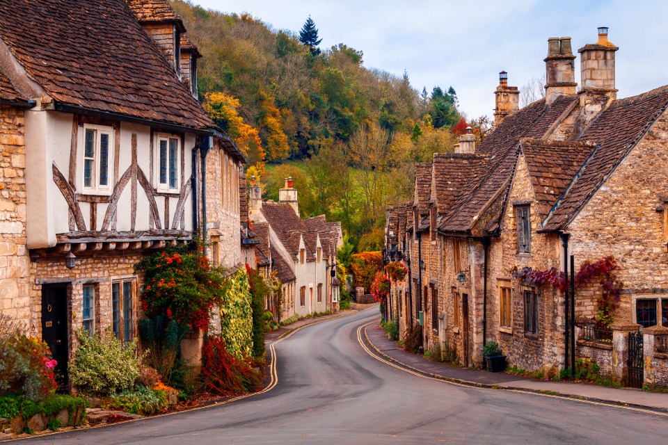 Stone houses line a curving road in Castle Combe, Wiltshire, England during autumn.