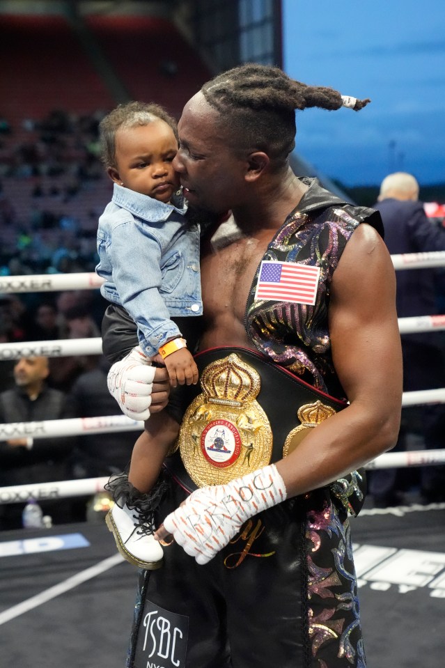 A boxer holds his child and championship belt after a win.