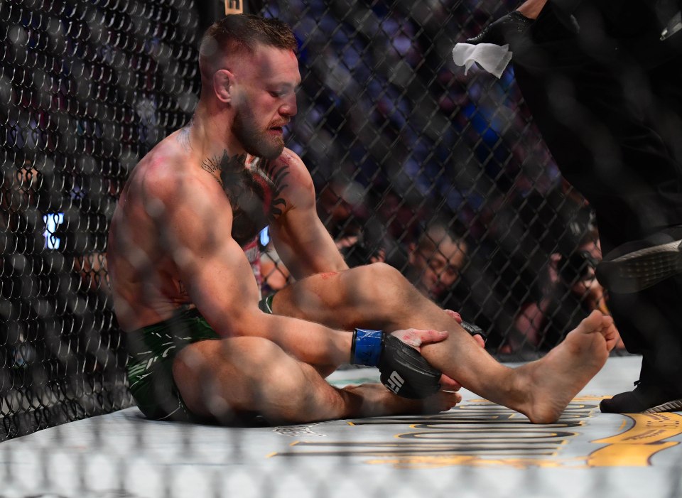 Conor McGregor holding his injured leg in the octagon.