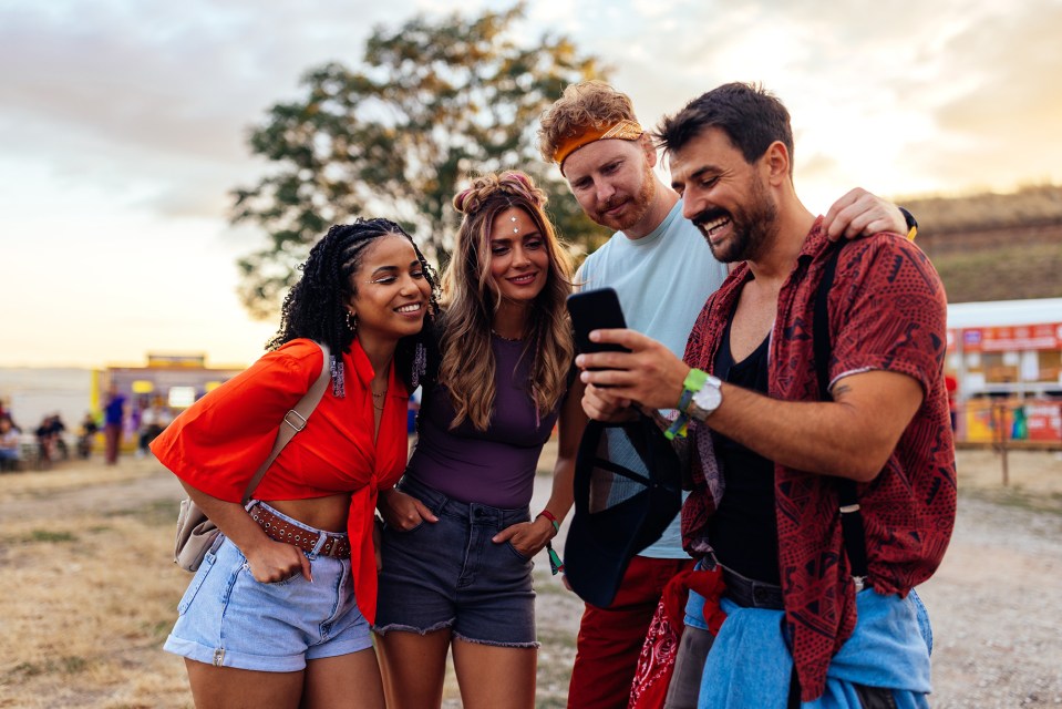 Four friends looking at a smartphone together at a festival.