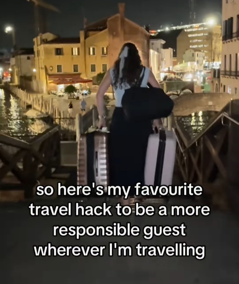 Woman pulling luggage across a bridge at night.