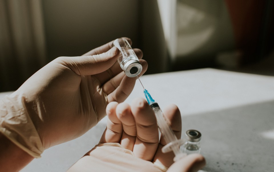 Gloved hands drawing medicine into a syringe from a vial.