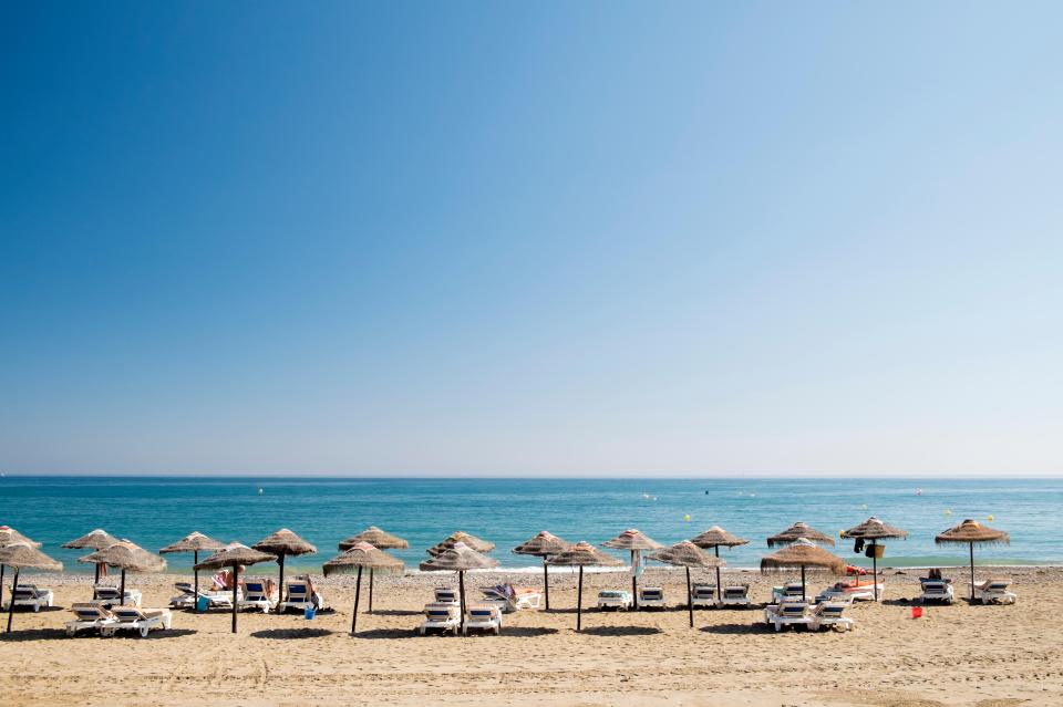 Beach with thatched umbrellas and lounge chairs.