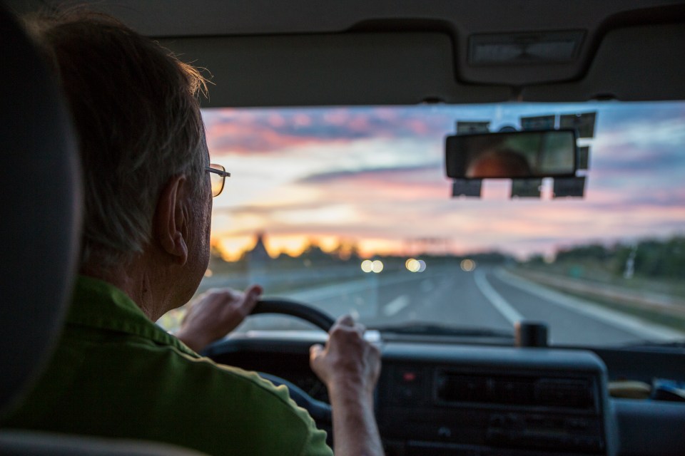 Senior man driving at sunset.