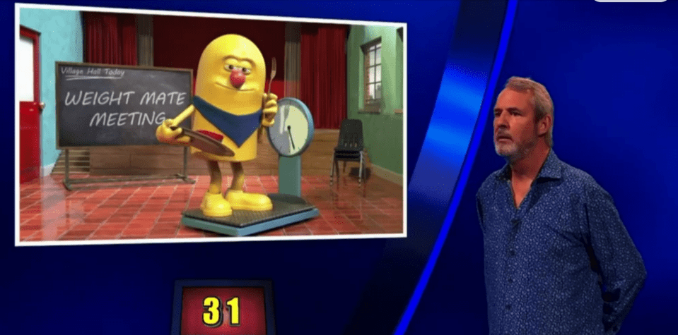 Screenshot of a game show featuring an animated character on a scale at a weight-mate meeting and a man standing beside the screen.