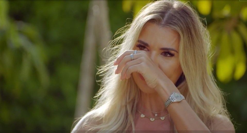 Screenshot of a blonde woman crying, covering her face with her hand.