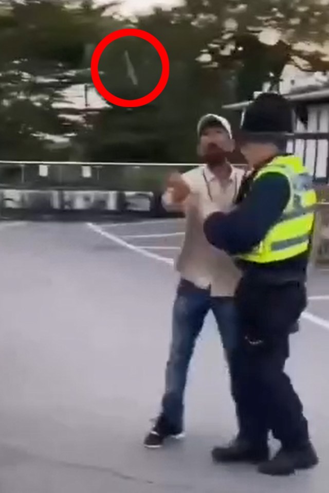 An asylum seeker flips off protesters while being escorted by police.