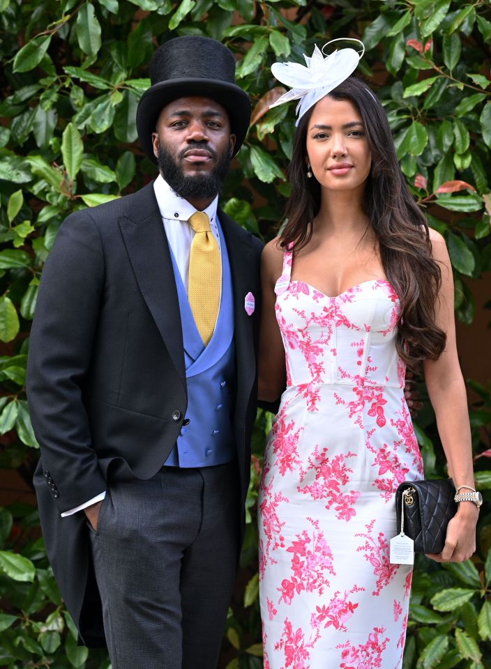A man in a top hat and woman in a floral dress stand together.