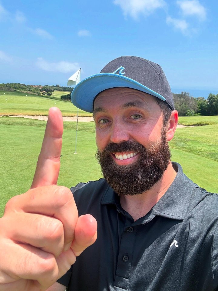 Man on golf course holding up index finger.