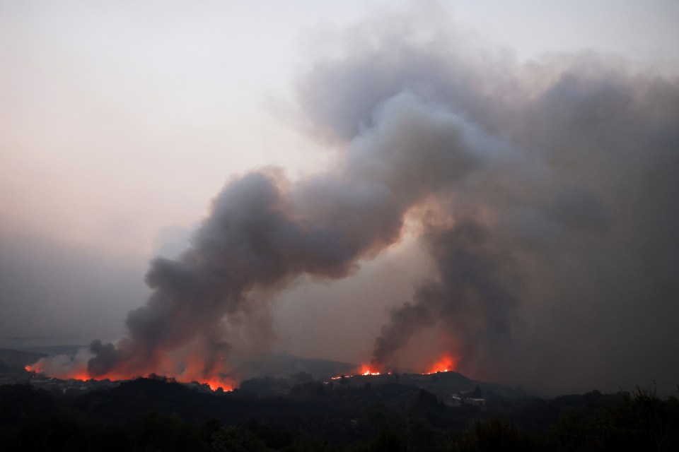 Wildfire smoke billows over a landscape.