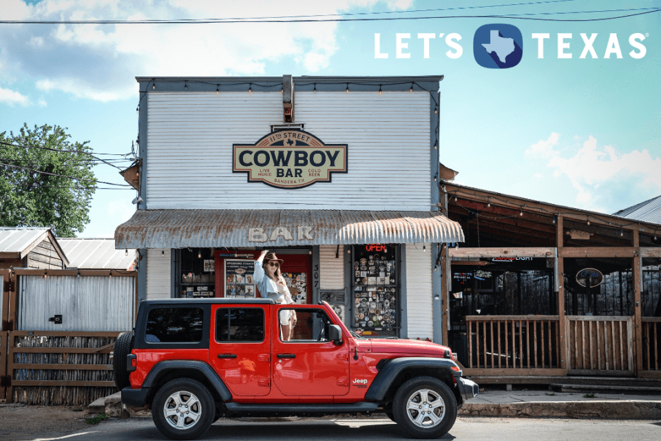 Woman in a red Jeep parked in front of the Cowboy Bar in Bandera, Texas.