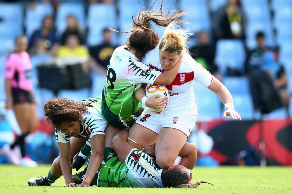 A rugby player from England is tackled by two players from the Cook Islands during a Women's Rugby League World Cup match.