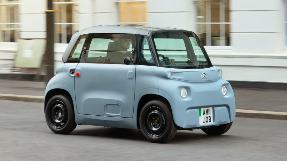 Light blue Citroën Ami driving on a blurred street.