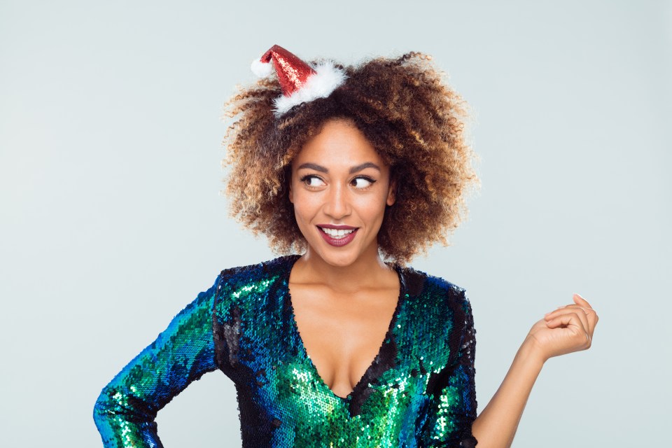 Portrait of a smiling young woman wearing a sequined dress and Santa hat.