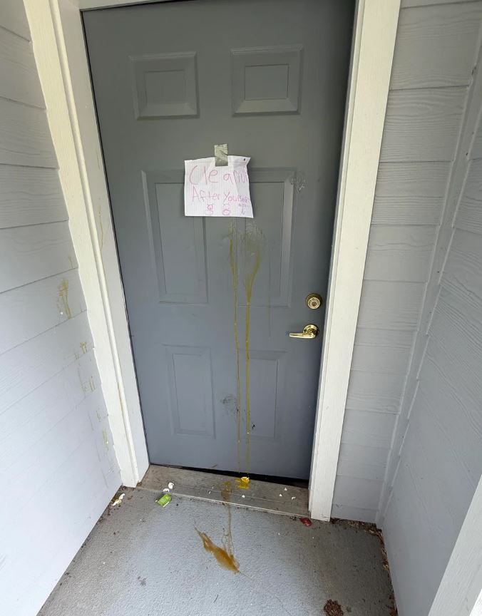 A door with a note saying "Clean After Yourself" and a mess on the floor.