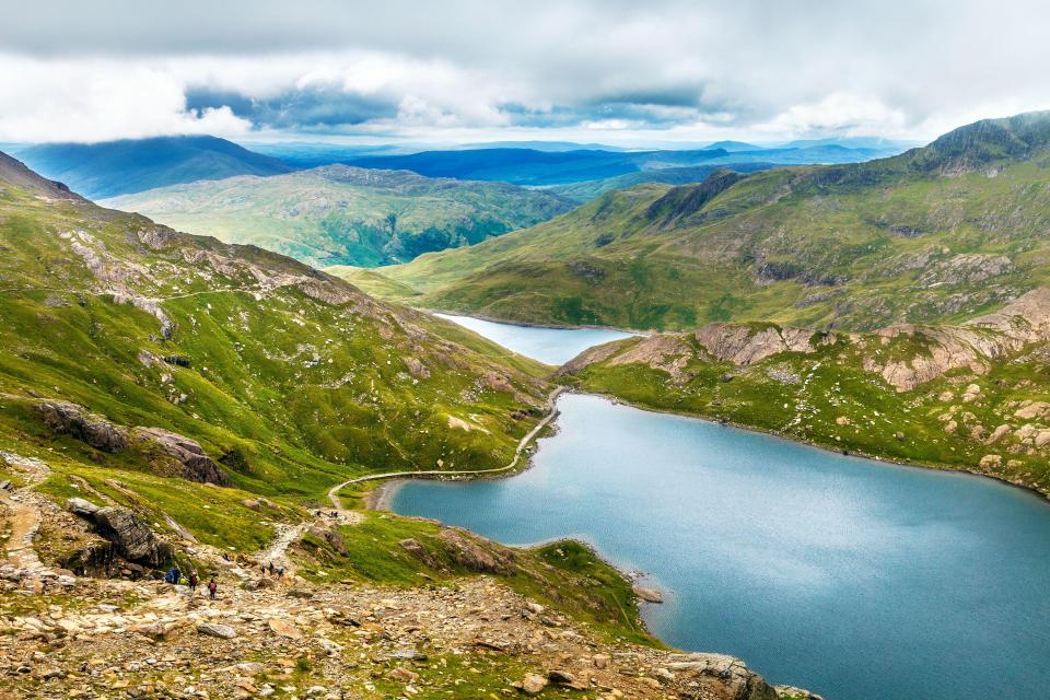 Hikers on a mountain trail overlooking Glaslyn and Llyn Llydaw lakes in Snowdonia National Park.