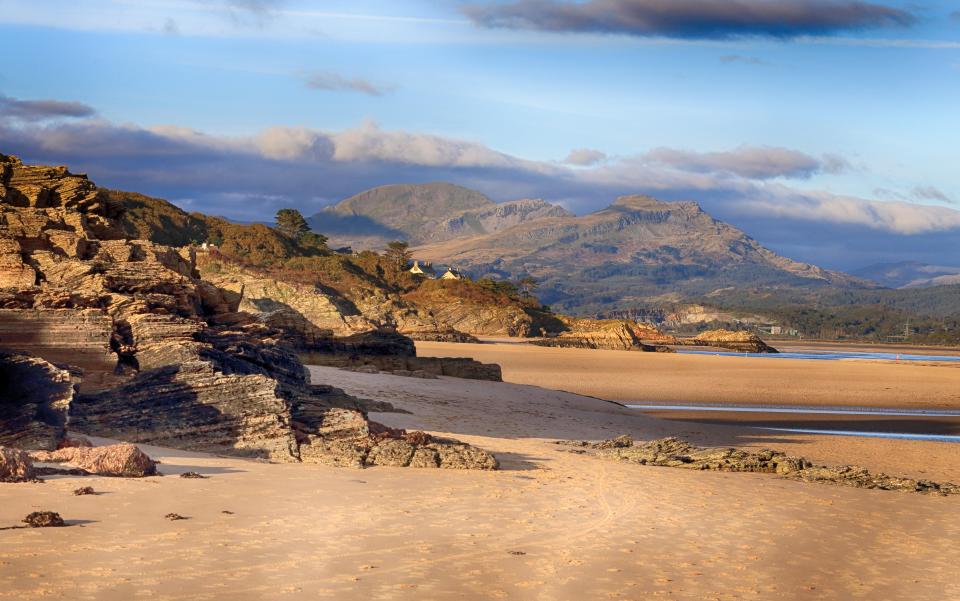 Sandy beach with rocky cliffs and mountains in the background.