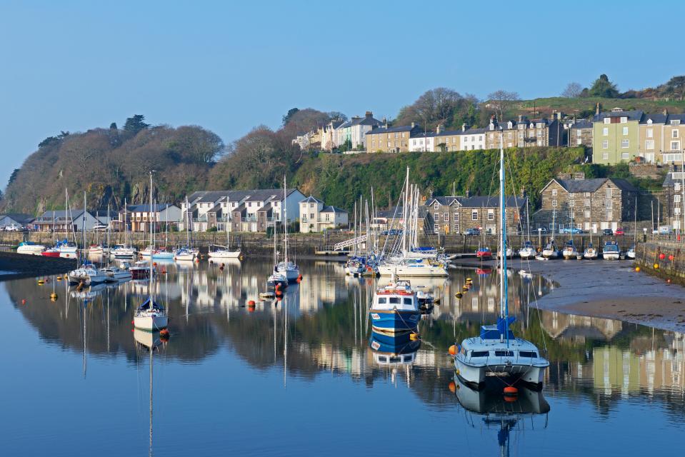 Porthmadog harbor in North Wales, UK, with boats moored and reflected in the calm water.