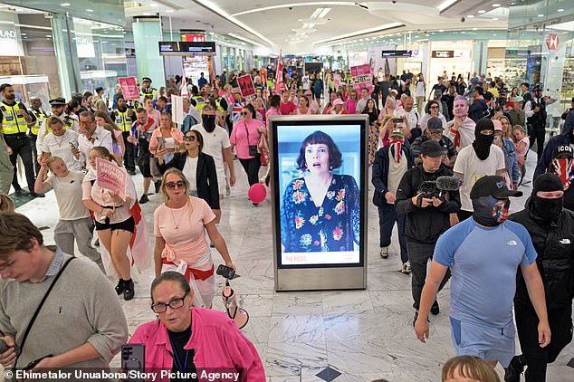 A crowd of masked protesters have clashed with police at a Canary Wharf shopping centre today with a police officer being 'punched in the face'.