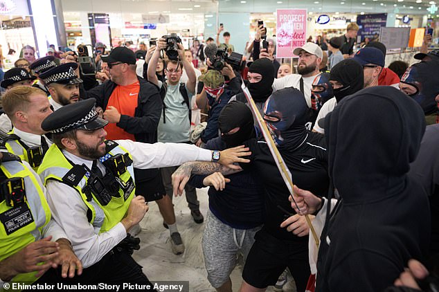 Masked protesters clash with police as they make their way through the shopping centre in the Isle of Dogs