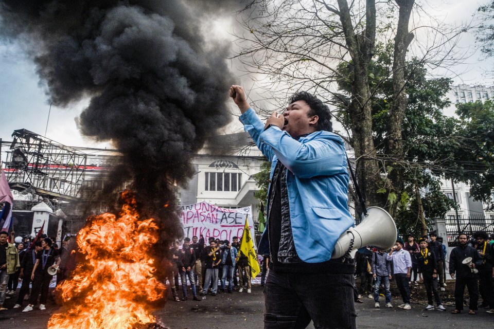 A protester shouts into a megaphone at a demonstration in Bandung, Indonesia, with a fire burning in the background.