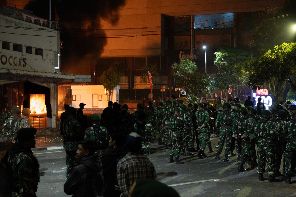 Soldiers standing guard near burning buildings during protests in Surabaya, Indonesia.