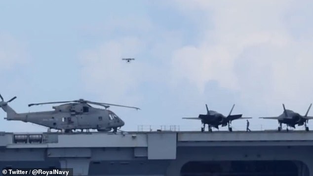 The drone is seen flying from the flight deck of HMS Prince of Wales, soaring above some of the warship's embarked airwing of helicopters and F-35 stealth jets
