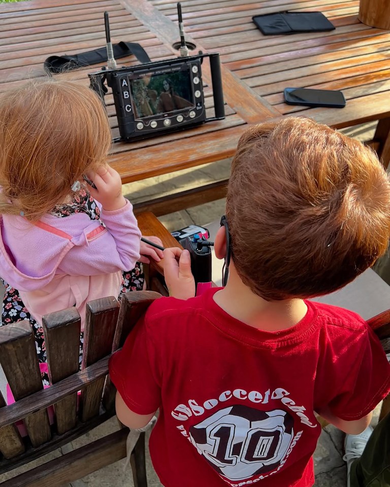 Two young children watching a video monitor on a wooden table.