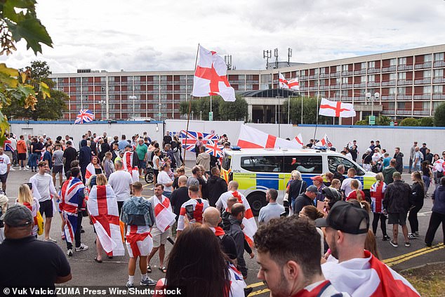 Protestors outside the Crowne Hotel adorned in England flags as a police van patrols the scene