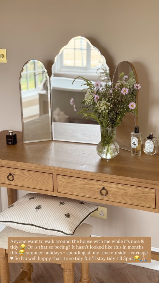 A tidy vanity with a tri-fold mirror, flowers, and perfume.