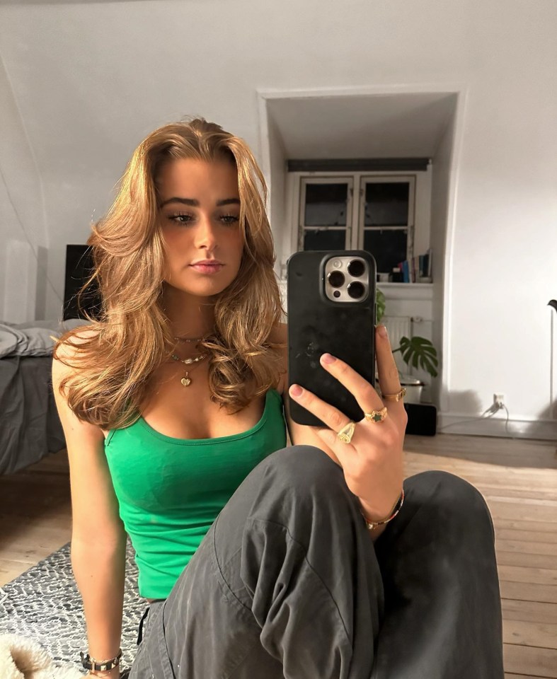 Selfie of a young woman wearing a green tank top and dark pants.