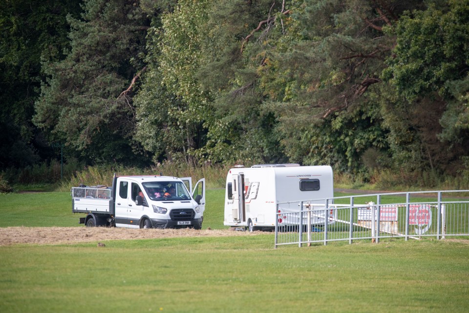 A white van and caravan parked in a park.