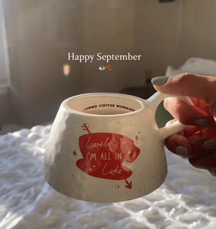 Hand holding a coffee mug that says "Lorelai, I'm all in Luke".
