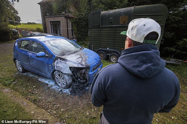 The owner of a vehicle looks on at its burnt remains after cars were set on fire in Ballymena, Co Antrim on Sunday