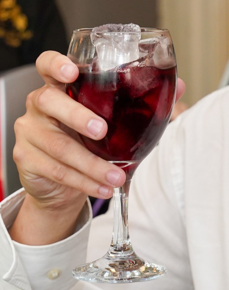 A hand holding a glass of red wine with ice.