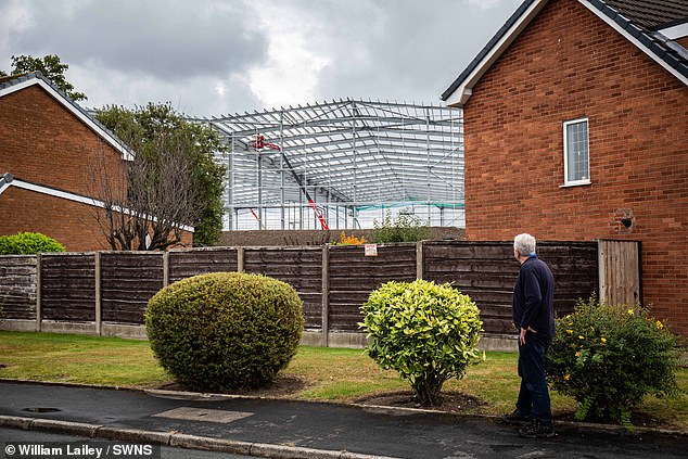 The council has agreed to a maximum height of 18.3m (60ft) for two of the buildings (pictured: John Peters gazes up at the frame)