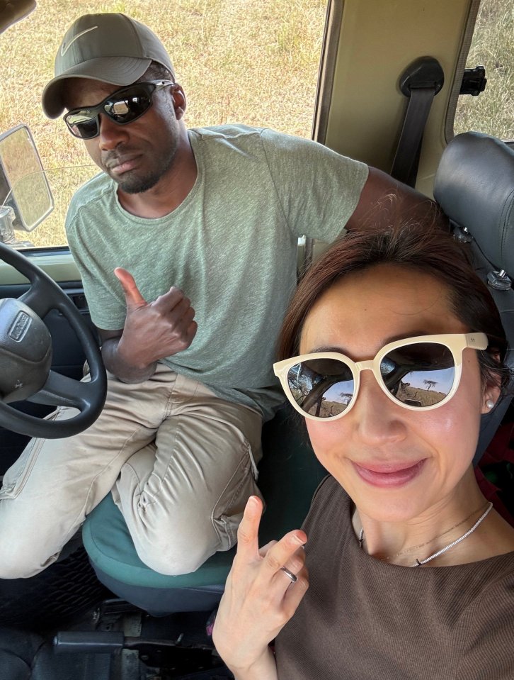 A woman and a man sitting in a safari vehicle; the man gives a thumbs up.