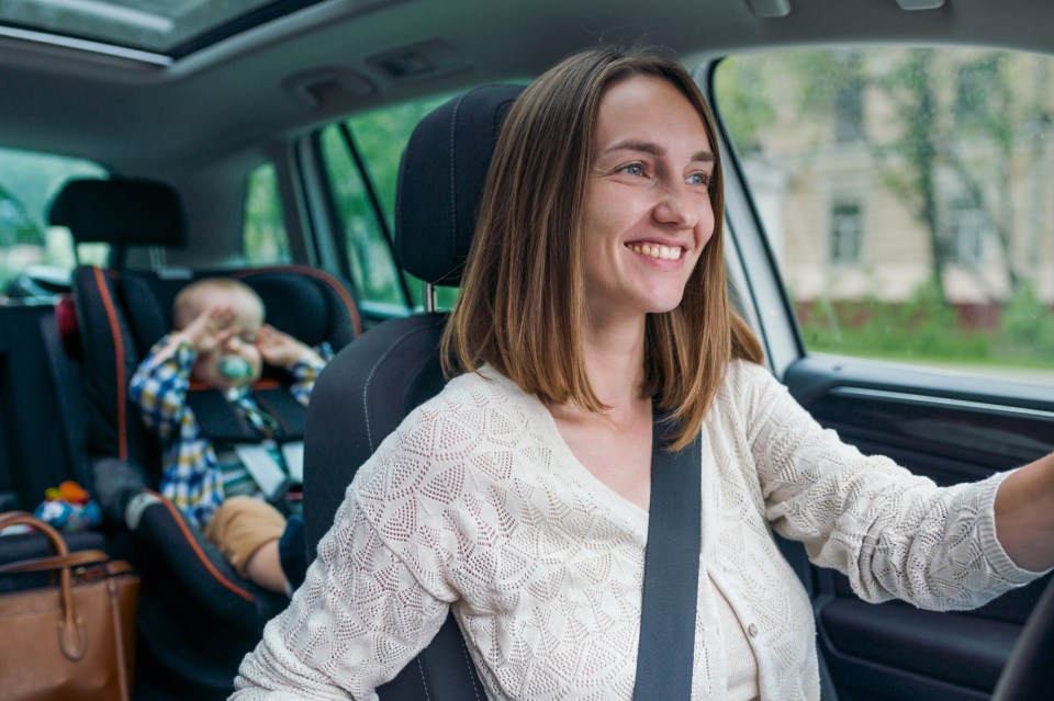 Beautiful smiling woman driving a car with little baby on the backseat