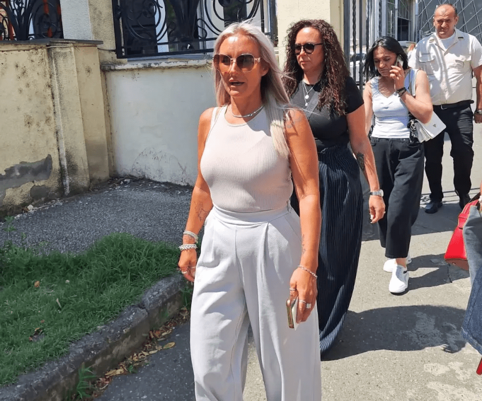 Woman in light gray pants and top walking with other people.