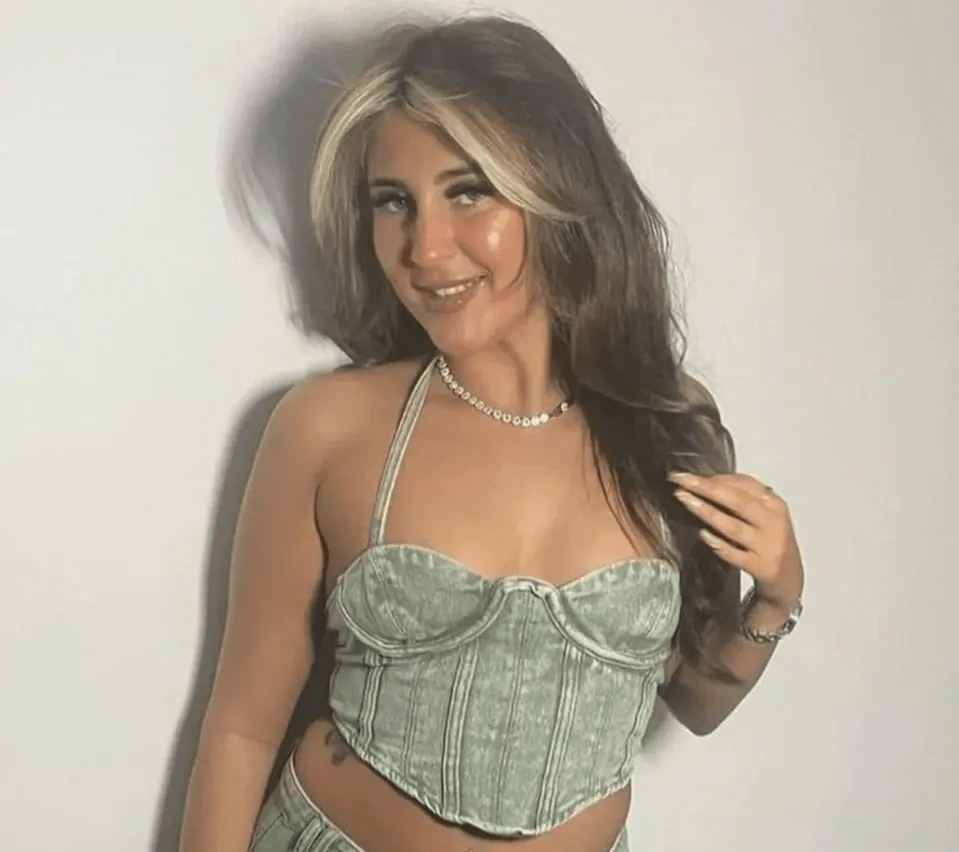 Woman with brown hair and highlights wearing a green denim corset top.