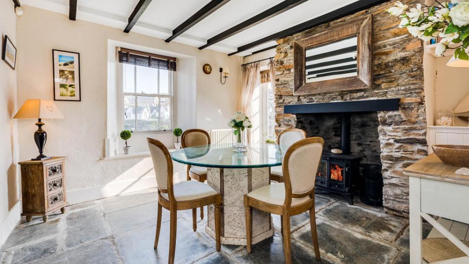 Dining area of Doc Martin's cottage with stone fireplace and glass-topped table.