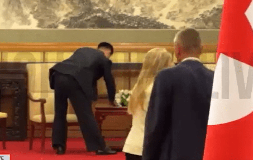 A man in a suit bending down to place flowers on a table.