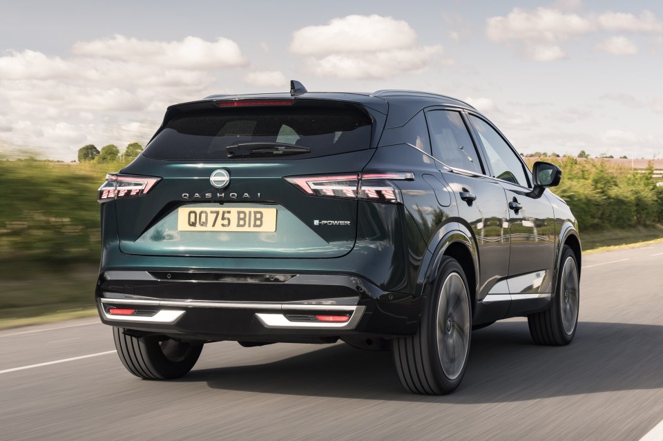 Rear view of a dark green Nissan Qashqai driving on a road.