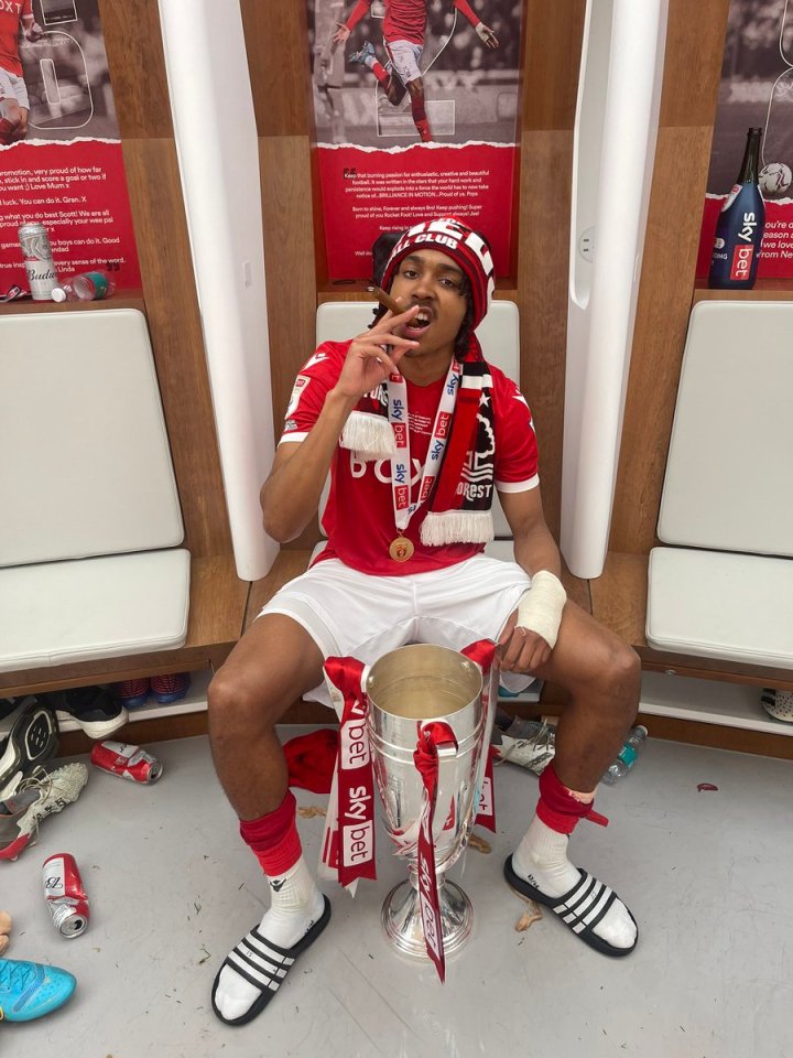 Djed Spence holding a trophy and smoking a cigar in a locker room.